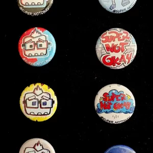 Assorted 1 inch Super Not Okay pins with various logos and designs